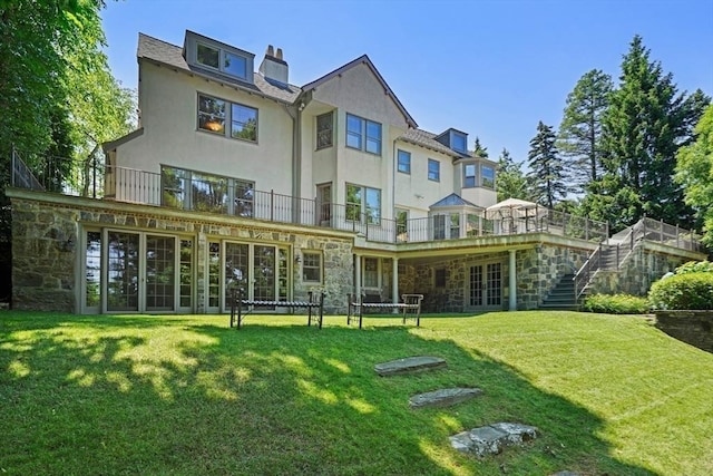 back of property featuring a chimney, stucco siding, a lawn, stone siding, and stairs