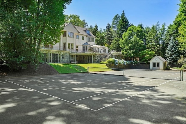 view of tennis court with a lawn and stairway