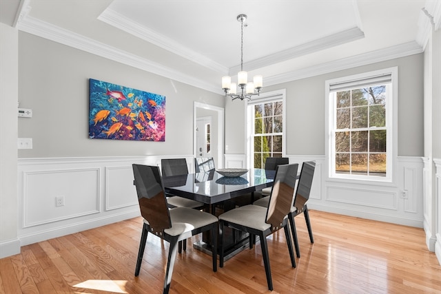 dining space featuring a raised ceiling, light hardwood / wood-style flooring, ornamental molding, and a notable chandelier