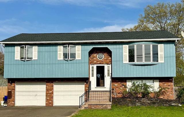 raised ranch with brick siding, driveway, an attached garage, and a shingled roof
