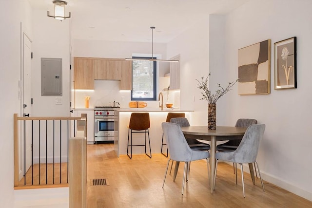 dining area with light wood-type flooring, electric panel, visible vents, and baseboards