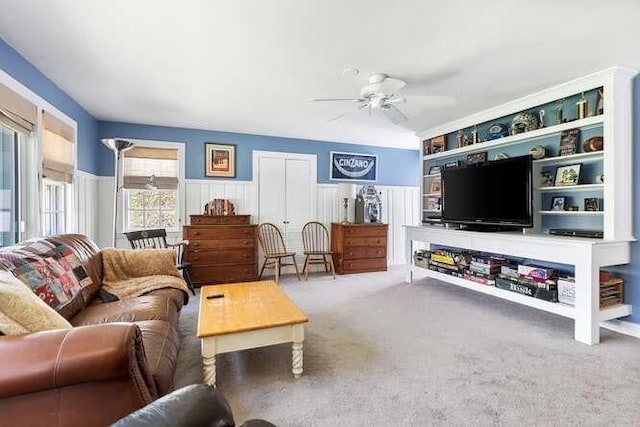 living area featuring carpet flooring, a ceiling fan, and a wainscoted wall