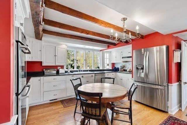 kitchen featuring dark countertops, beam ceiling, a chandelier, stainless steel appliances, and under cabinet range hood