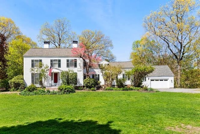 colonial-style house with an attached garage, a chimney, driveway, and a front yard
