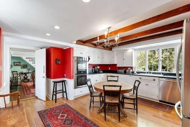 kitchen featuring white cabinets, beamed ceiling, light wood finished floors, a chandelier, and stainless steel appliances