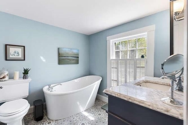 bathroom with baseboards, vanity, toilet, and a soaking tub