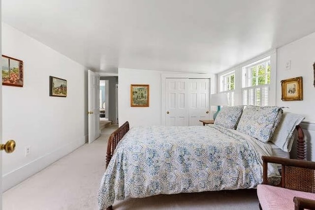 bedroom with baseboards, light colored carpet, and a closet