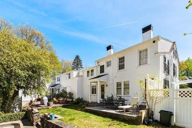 back of property featuring fence, a patio, a chimney, and a yard