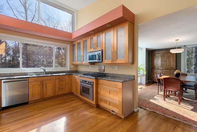 kitchen featuring a sink, glass insert cabinets, appliances with stainless steel finishes, dark countertops, and light wood-type flooring