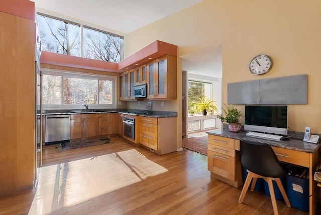 kitchen with dark countertops, glass insert cabinets, open floor plan, light wood-type flooring, and appliances with stainless steel finishes