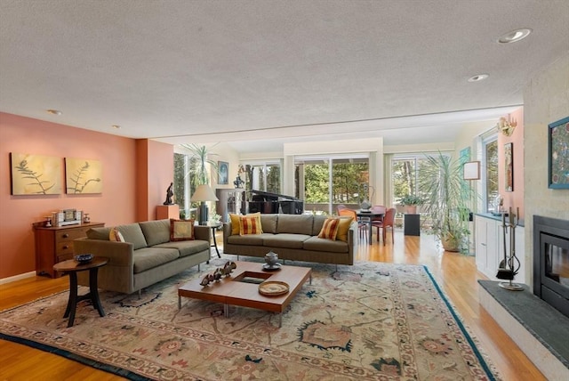 living room featuring a textured ceiling, light wood-style flooring, baseboards, and a large fireplace