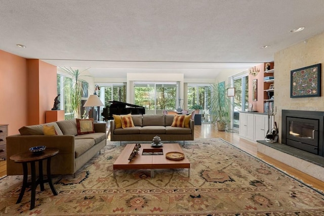 living area with built in features, a textured ceiling, a large fireplace, and wood finished floors