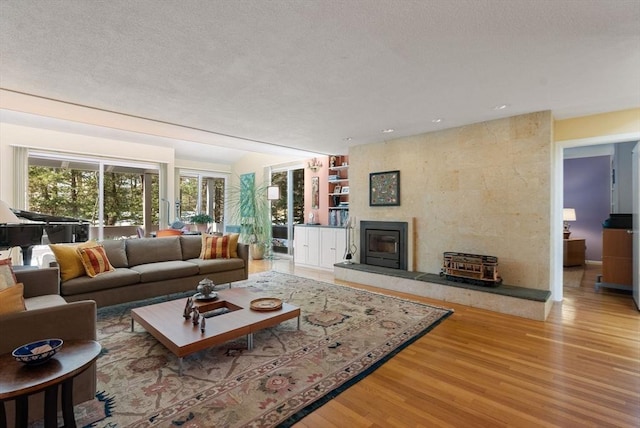 living area with built in shelves, a large fireplace, a textured ceiling, and wood finished floors