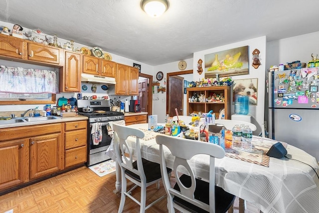 kitchen featuring light countertops, under cabinet range hood, brown cabinets, a sink, and stainless steel appliances