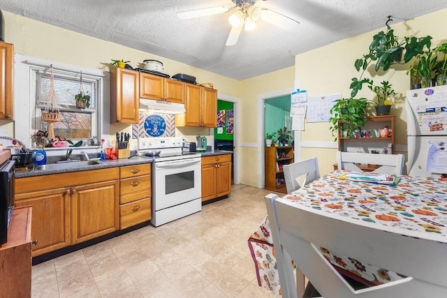 kitchen with brown cabinets, dark countertops, white appliances, a ceiling fan, and under cabinet range hood