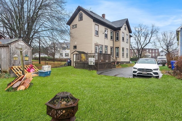 view of side of property featuring an outdoor fire pit, a wooden deck, a shed, a chimney, and a lawn