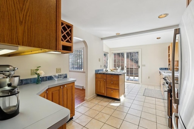 kitchen with light tile patterned floors, arched walkways, lofted ceiling, a sink, and brown cabinets