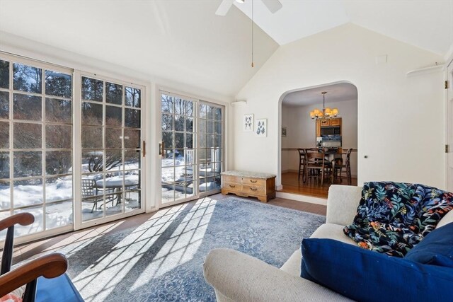 living area featuring lofted ceiling, arched walkways, and ceiling fan with notable chandelier