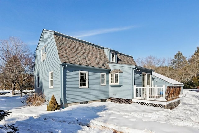 snow covered rear of property with a shingled roof, a deck, and a gambrel roof