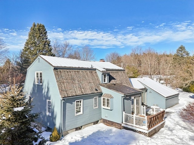 snow covered back of property featuring a wooden deck, a chimney, a shingled roof, and a gambrel roof