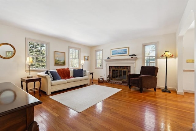 living area with hardwood / wood-style floors, a brick fireplace, and baseboards