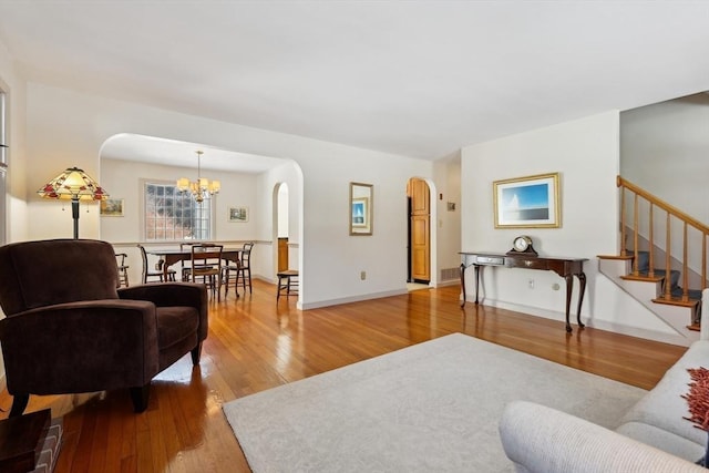 living room with arched walkways, hardwood / wood-style flooring, a notable chandelier, baseboards, and stairway