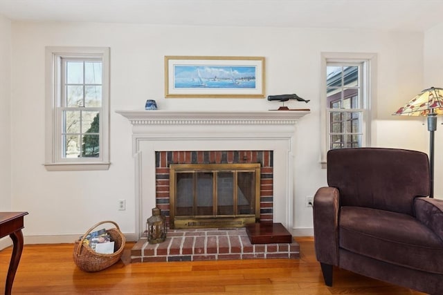 living area with a brick fireplace, baseboards, and wood finished floors