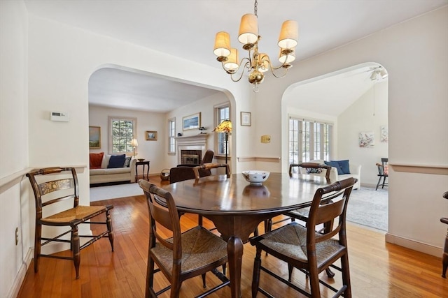 dining room featuring plenty of natural light, a fireplace, a chandelier, and wood finished floors