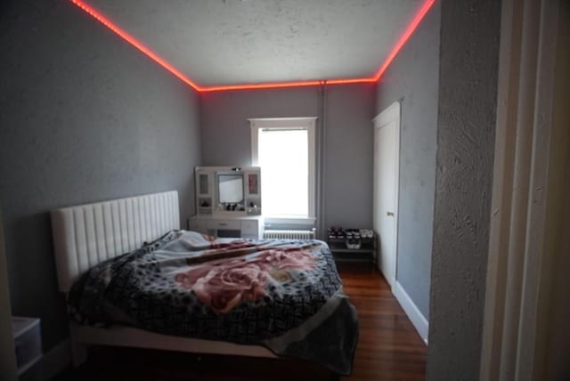 bedroom with a textured wall, radiator heating unit, and wood finished floors