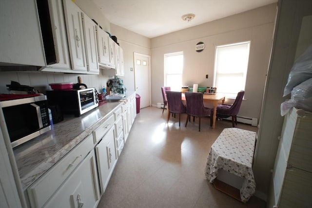 kitchen with stainless steel microwave, white cabinets, light flooring, light countertops, and baseboard heating