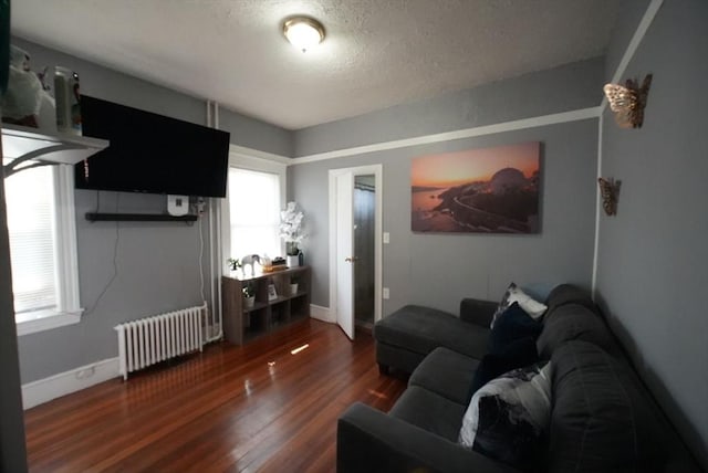 living area with radiator heating unit, wood finished floors, a textured ceiling, and baseboards