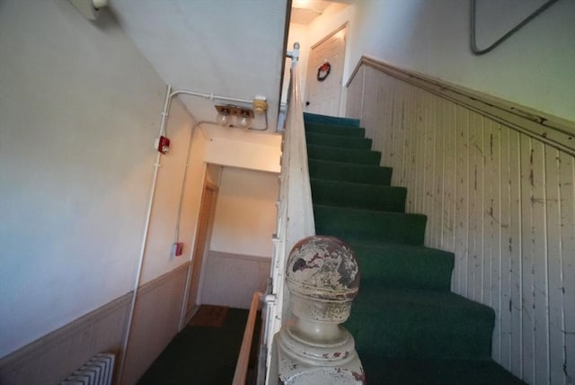 stairway with a wainscoted wall, wood walls, and radiator heating unit