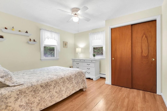 bedroom featuring multiple windows, light wood-type flooring, a baseboard heating unit, and a closet