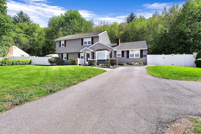 colonial home featuring a chimney, a gate, and driveway