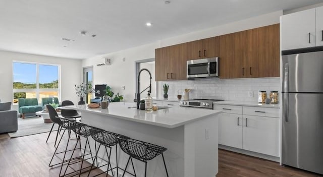 kitchen featuring tasteful backsplash, light countertops, appliances with stainless steel finishes, a kitchen breakfast bar, and a sink