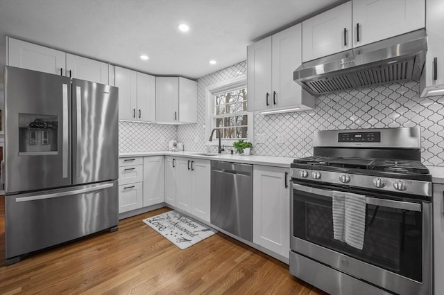 kitchen featuring exhaust hood, light wood-type flooring, white cabinets, stainless steel appliances, and backsplash