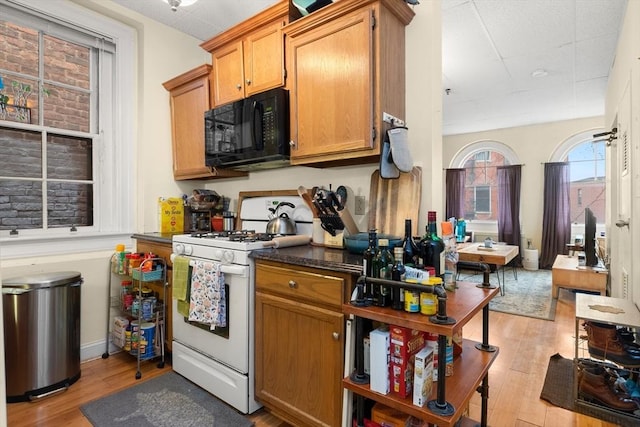 kitchen featuring light wood-style floors, dark countertops, white gas range, and black microwave
