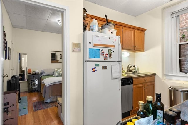 kitchen with brown cabinets, freestanding refrigerator, a sink, and stainless steel dishwasher