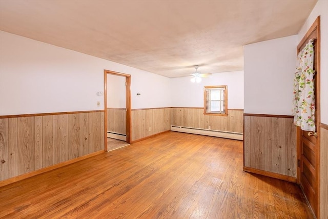 empty room featuring a baseboard radiator, wooden walls, ceiling fan, and light hardwood / wood-style flooring