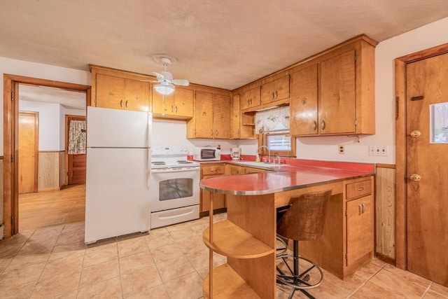 kitchen with wood walls, sink, a kitchen bar, kitchen peninsula, and white appliances