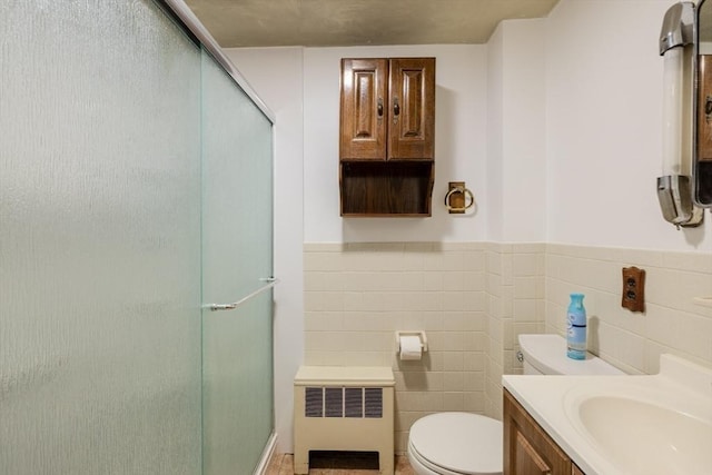 bathroom featuring toilet, a shower with shower door, tile walls, radiator heating unit, and vanity