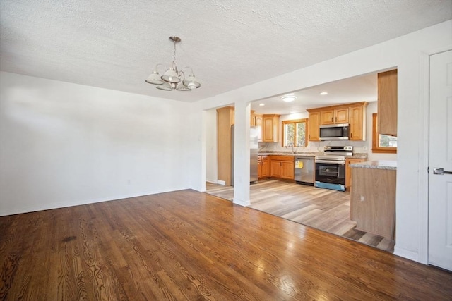 kitchen with sink, an inviting chandelier, light hardwood / wood-style flooring, hanging light fixtures, and appliances with stainless steel finishes