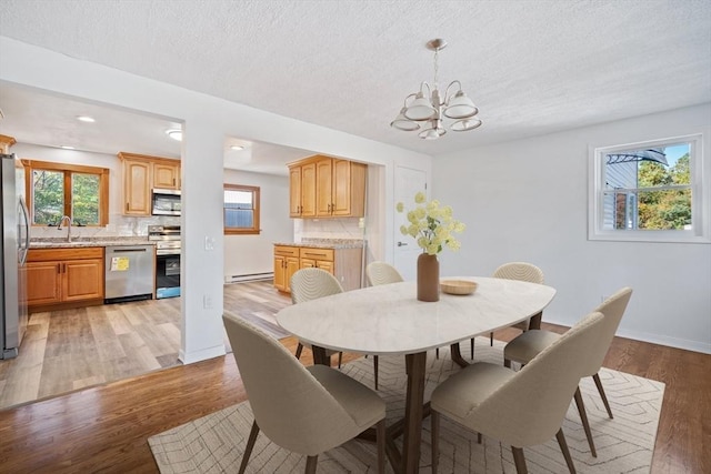 dining room with a textured ceiling, a baseboard heating unit, an inviting chandelier, sink, and light hardwood / wood-style flooring