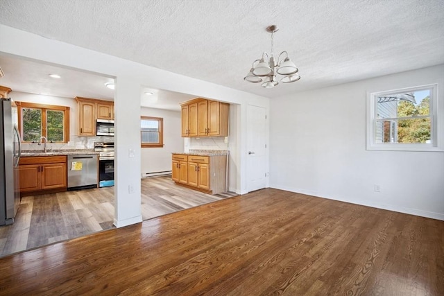 kitchen with tasteful backsplash, hanging light fixtures, light wood-type flooring, stainless steel appliances, and a baseboard radiator