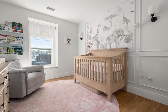 bedroom featuring a crib, light wood-style flooring, and visible vents