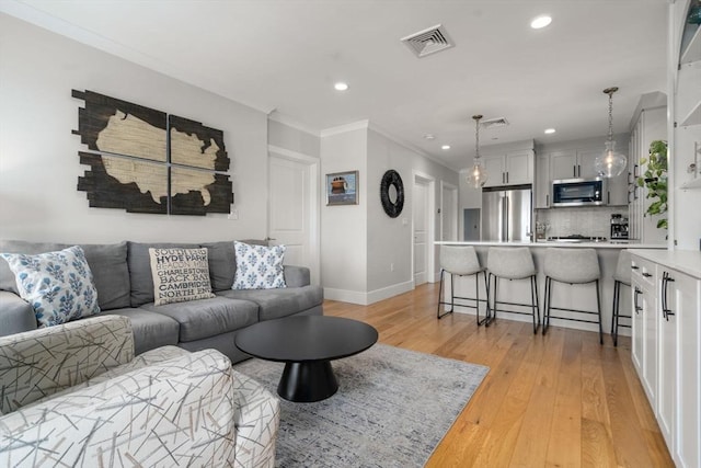 living area featuring visible vents, crown molding, baseboards, recessed lighting, and light wood-style flooring