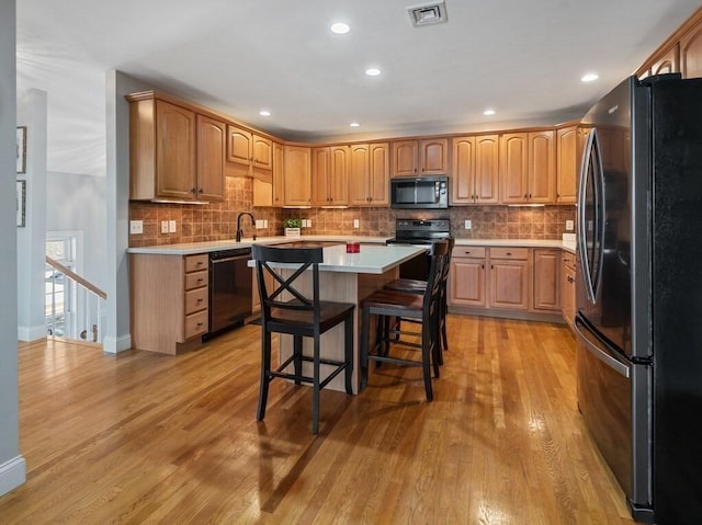 kitchen featuring visible vents, a kitchen island, a kitchen breakfast bar, light countertops, and black appliances