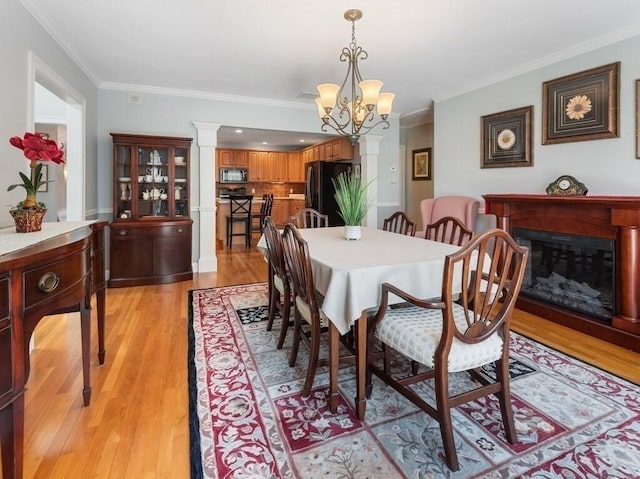 dining space with light wood-style floors, a glass covered fireplace, and ornamental molding