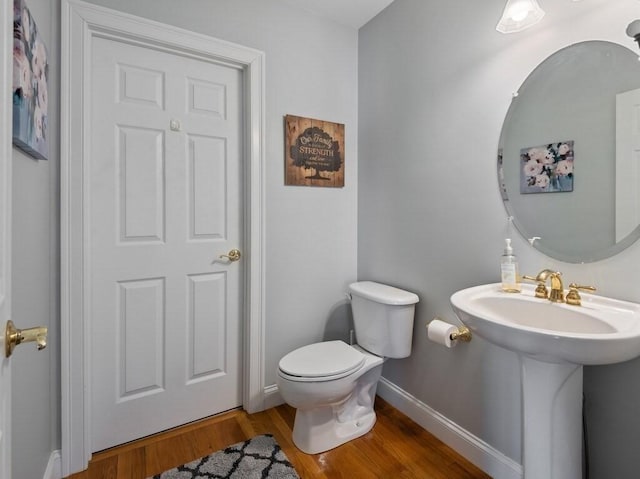 half bath featuring a sink, wood finished floors, toilet, and baseboards