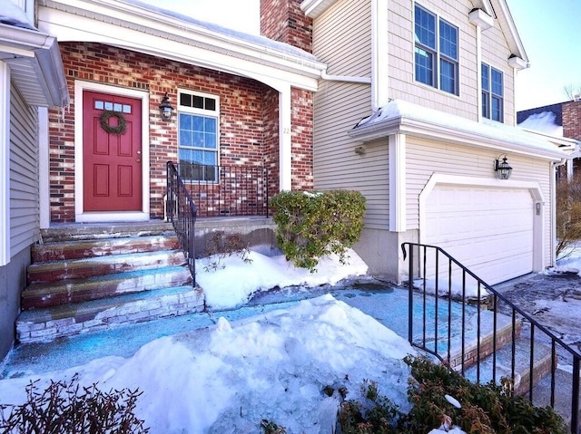 snow covered property entrance with brick siding, a chimney, and an attached garage